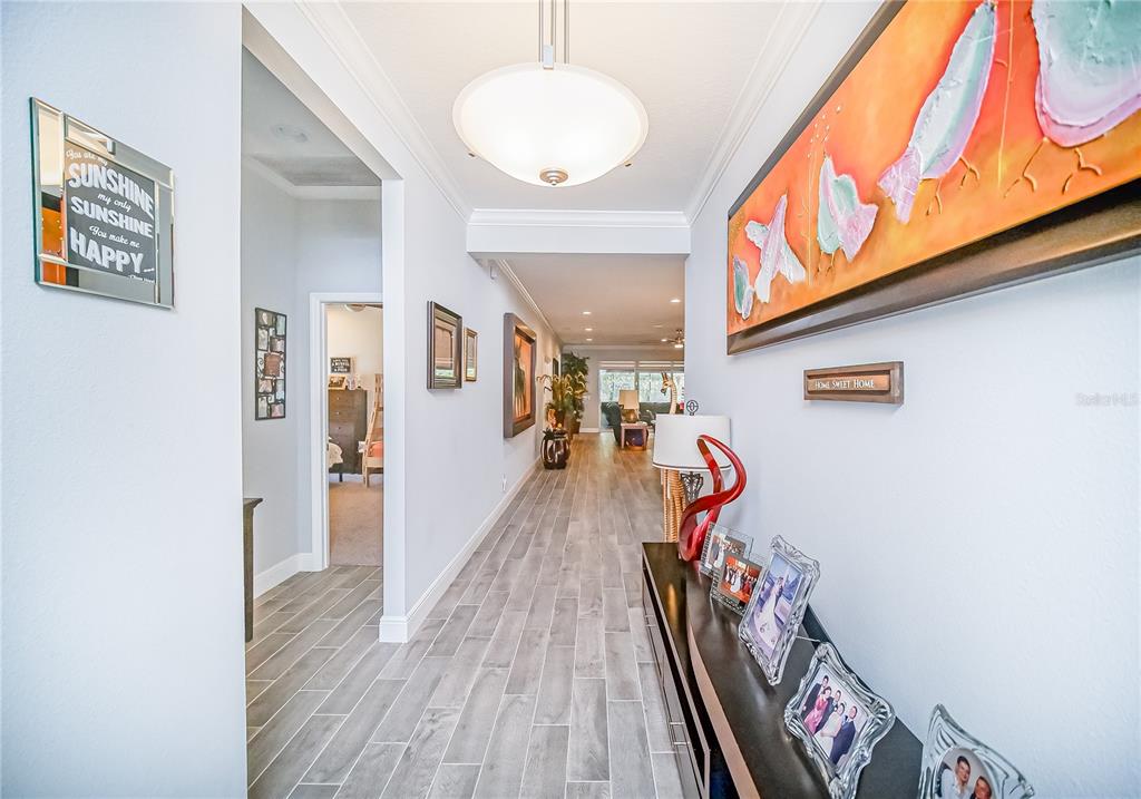 A bright hallway features wood-look tile flooring, a large pendant light, and framed wall art — 2389 PEARL CIDER STREET, ORLANDO, FL