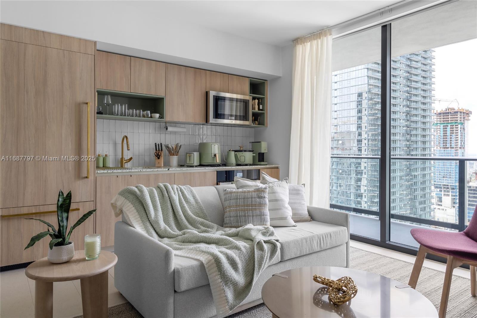 A modern studio apartment features a kitchenette with light wood cabinets and a sofa — 159 NE 6TH ST # 3002, Miami FL 33132, MIAMI, FL