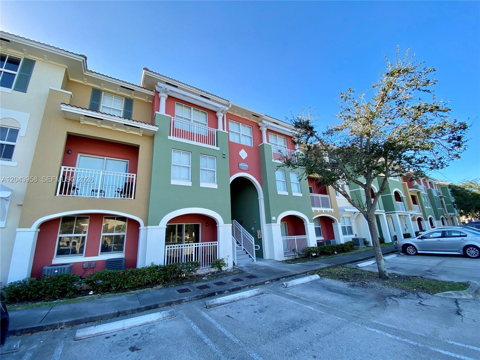 A multi-story apartment building features colorful stucco walls, arched entryways, and balconies under a blue sky — 11202 NW 83rd St # 106, Doral FL 33178, DORAL, FL