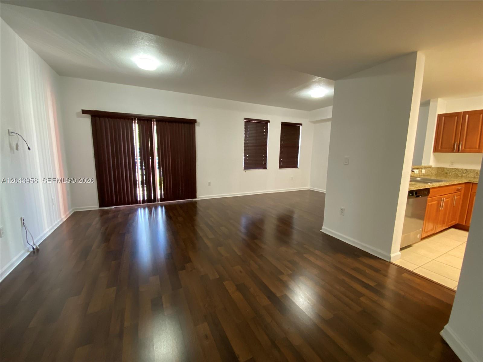 An open living area features dark wood flooring, vertical blinds, and an adjacent kitchen — 11202 NW 83rd St # 106, Doral FL 33178, DORAL, FL