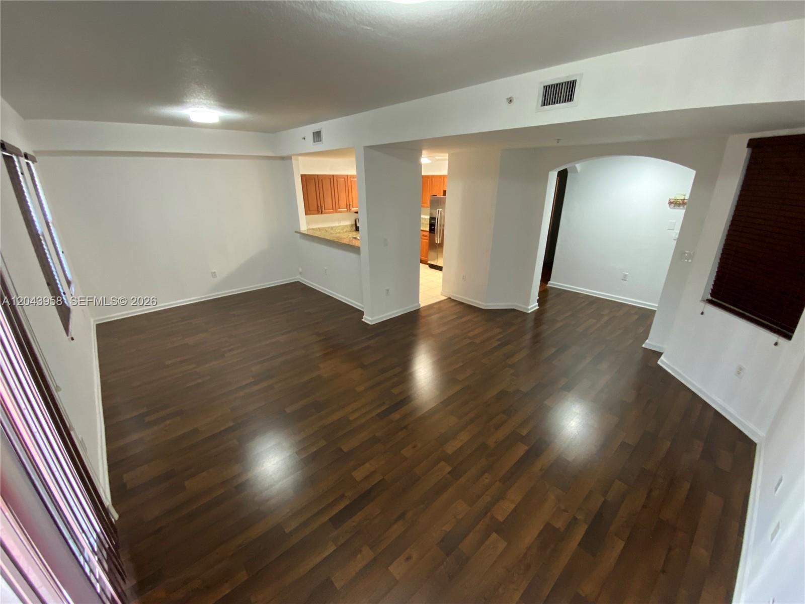 An empty living room features dark wood flooring, white walls, and an open kitchen area — 11202 NW 83rd St # 106, Doral FL 33178, DORAL, FL