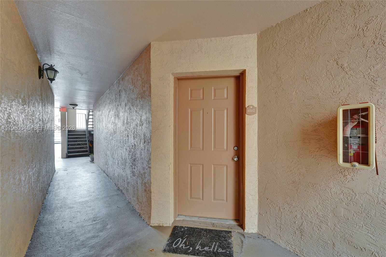 A tan door with a welcome mat sits in a concrete hallway with a fire extinguisher — 2846 S University Dr # 4102, Davie FL 33328, DAVIE, FL