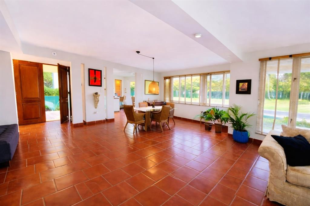 A spacious living and dining area features terracotta tile floors, large windows, and wooden doors — Principal E1 LAKESIDE VILLAS, VEGA ALTA, PR
