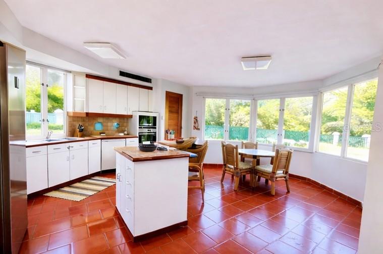 A kitchen and dining area with white cabinets, a center island, and red tile flooring — Principal E1 LAKESIDE VILLAS, VEGA ALTA, PR
