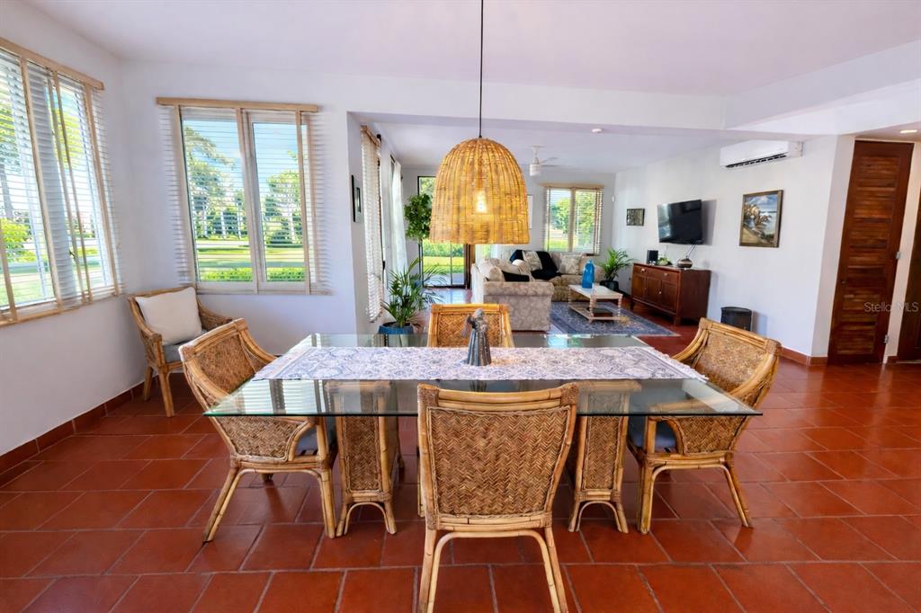 A dining area with a glass-top rattan table and chairs sits before an open living room — Principal E1 LAKESIDE VILLAS, VEGA ALTA, PR
