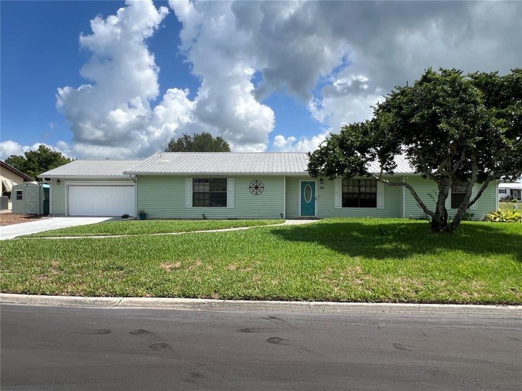 A light green single-story house with a metal roof, white garage, and a large tree — 530 MINNOW COURT, KENANSVILLE, FL