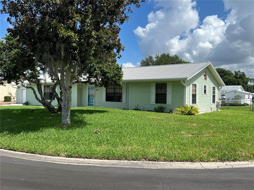 A light green, single-story house with a metal roof sits behind a large tree — 530 MINNOW COURT, KENANSVILLE, FL