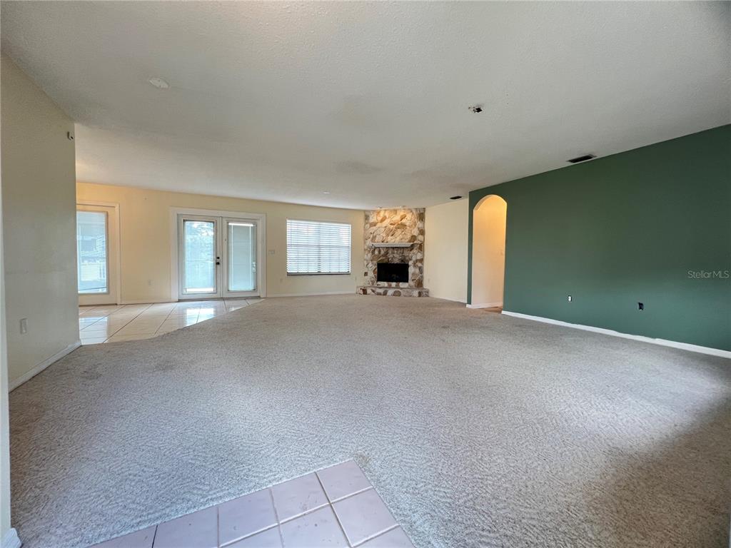 A spacious living room features beige carpeting, a stone fireplace, and a green accent wall — 530 MINNOW COURT, KENANSVILLE, FL