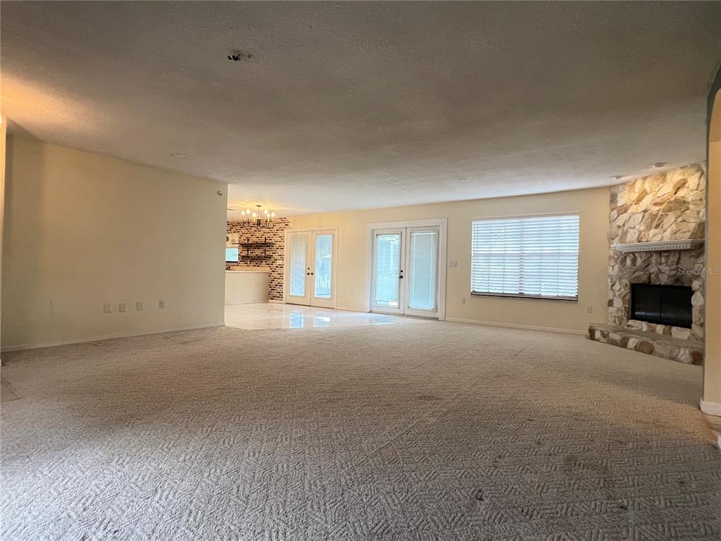 A spacious living room features beige carpeting, a stone fireplace, and French doors — 530 MINNOW COURT, KENANSVILLE, FL