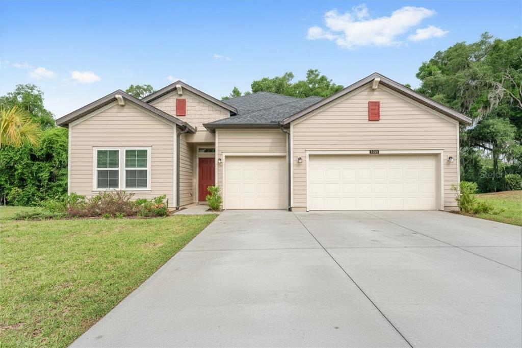 A tan single-story house with a three-car garage and a red front door — 19581 SW 77TH PLACE, DUNNELLON, FL