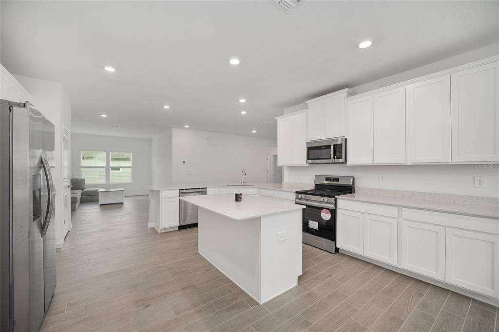 A modern kitchen features white cabinets, stainless steel appliances, a center island, and light flooring — 19581 SW 77TH PLACE, DUNNELLON, FL