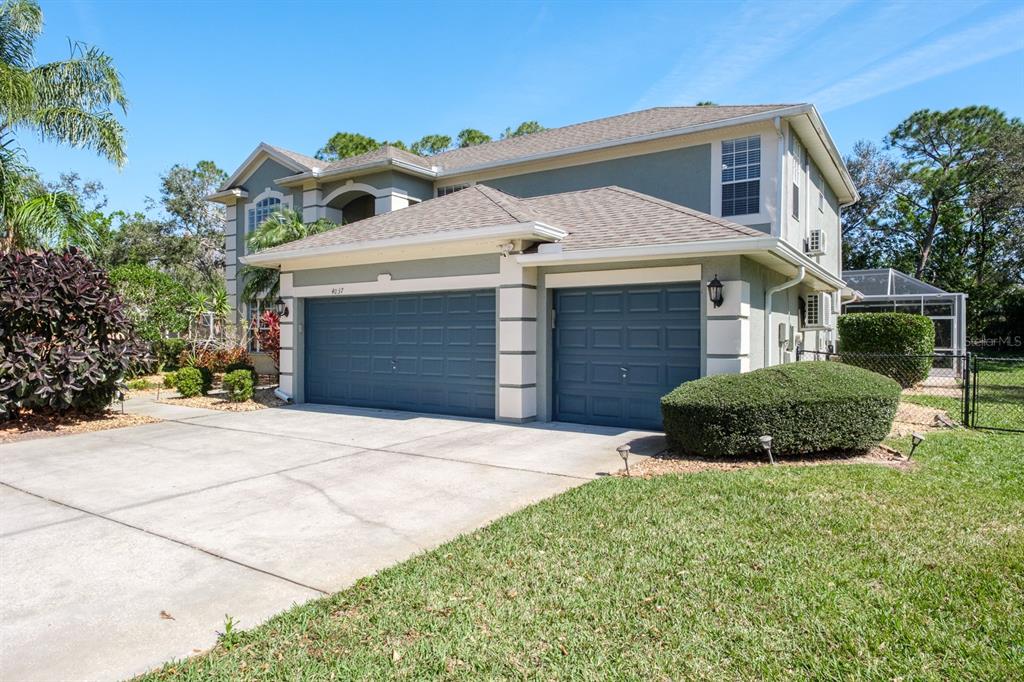 A two-story house with a three-car garage, light green siding, and a concrete driveway — 4037 AUSTON WAY, PALM HARBOR, FL