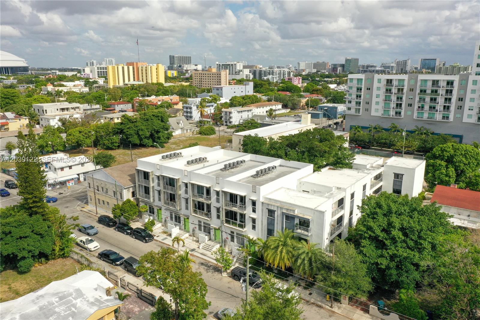 An aerial view shows a modern white multi-unit residential building surrounded by urban greenery — 761 NW 1st St, Miami FL 33128, MIAMI, FL