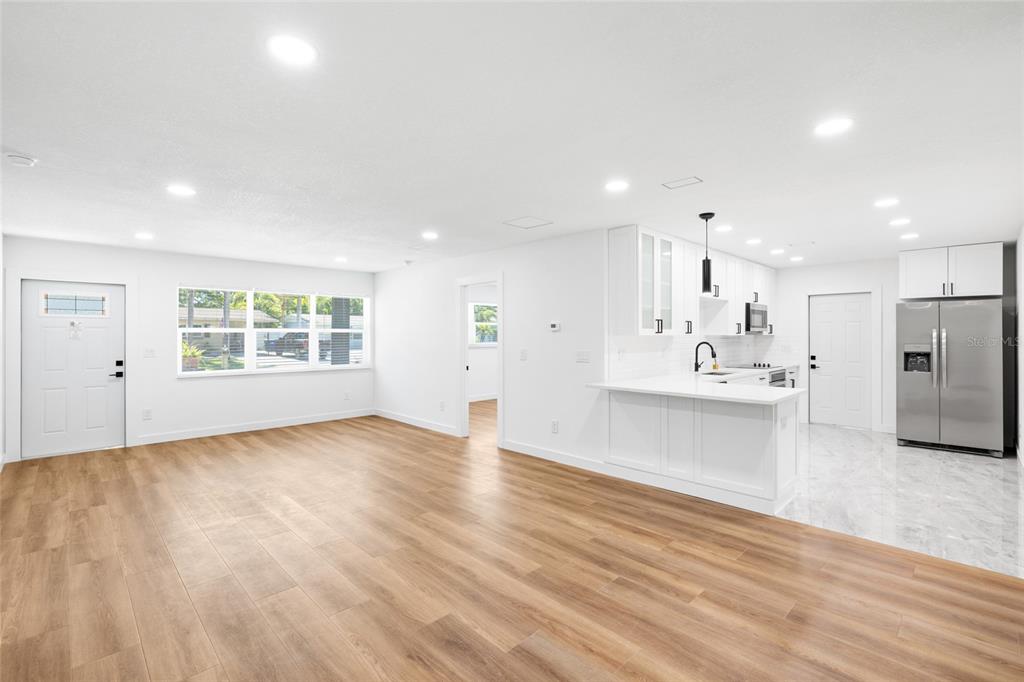 An open-concept living room and kitchen with wood-look flooring, white cabinets, and stainless appliances — 4513 S HESPERIDES STREET, TAMPA, FL