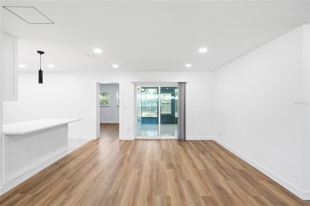 A bright, open-concept room features light wood-look flooring, white walls, and a sliding glass door — 4513 S HESPERIDES STREET, TAMPA, FL