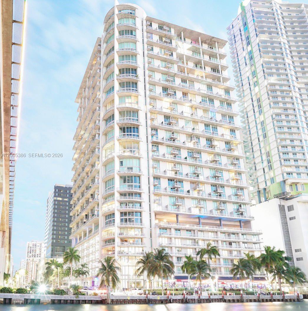 A modern high-rise apartment building stands along a waterfront with palm trees in the foreground — 690 SW 1st Ct # 2524, Miami FL 33130, MIAMI, FL