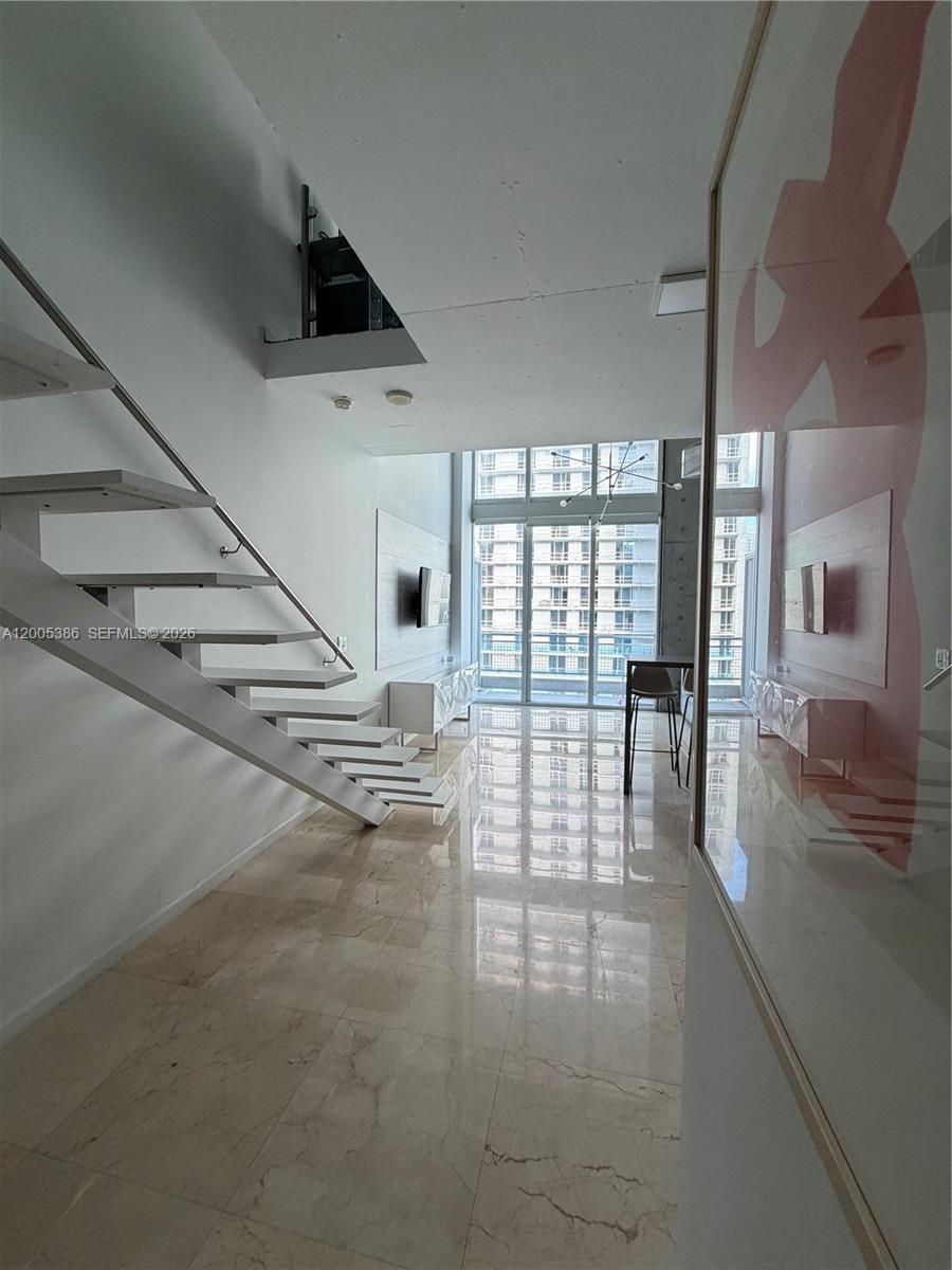 A modern living room features a floating staircase, marble floors, and floor-to-ceiling windows — 690 SW 1st Ct # 2524, Miami FL 33130, MIAMI, FL
