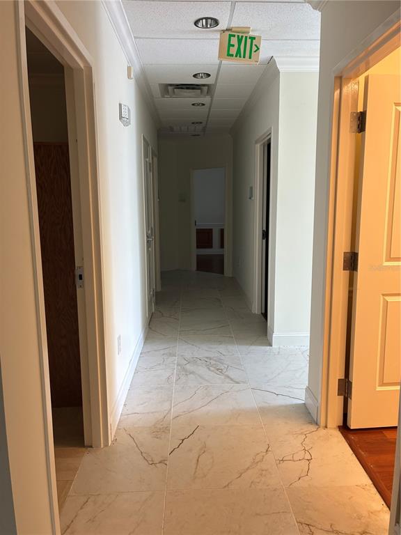 A hallway with white marble-style tile flooring leads to an exit sign and multiple doorways — 1350 CITY VIEW CENTER, OVIEDO, FL