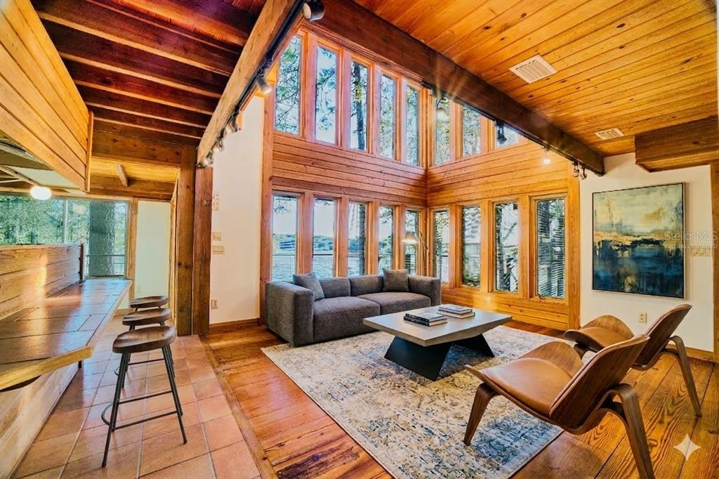 A living room with wood-paneled walls, a vaulted ceiling, floor-to-ceiling windows, and lake views — 123 MASON LAKE TRAIL, HAWTHORNE, FL