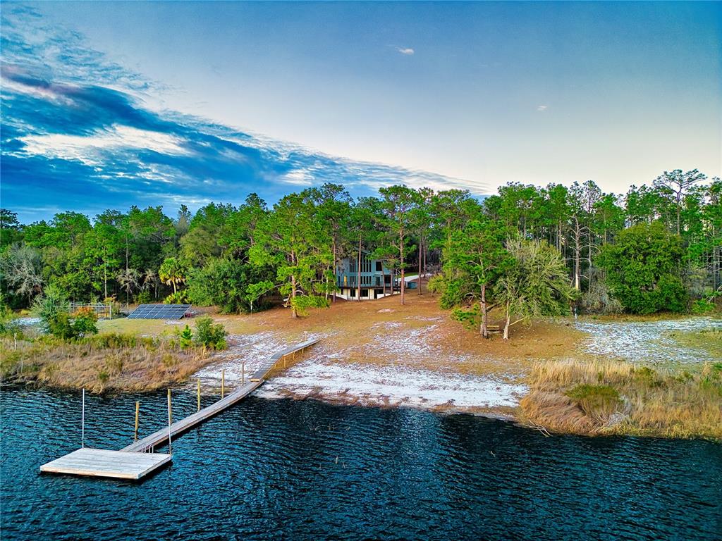 An aerial view shows a house nestled in trees with a dock extending into water — 123 MASON LAKE TRAIL, HAWTHORNE, FL
