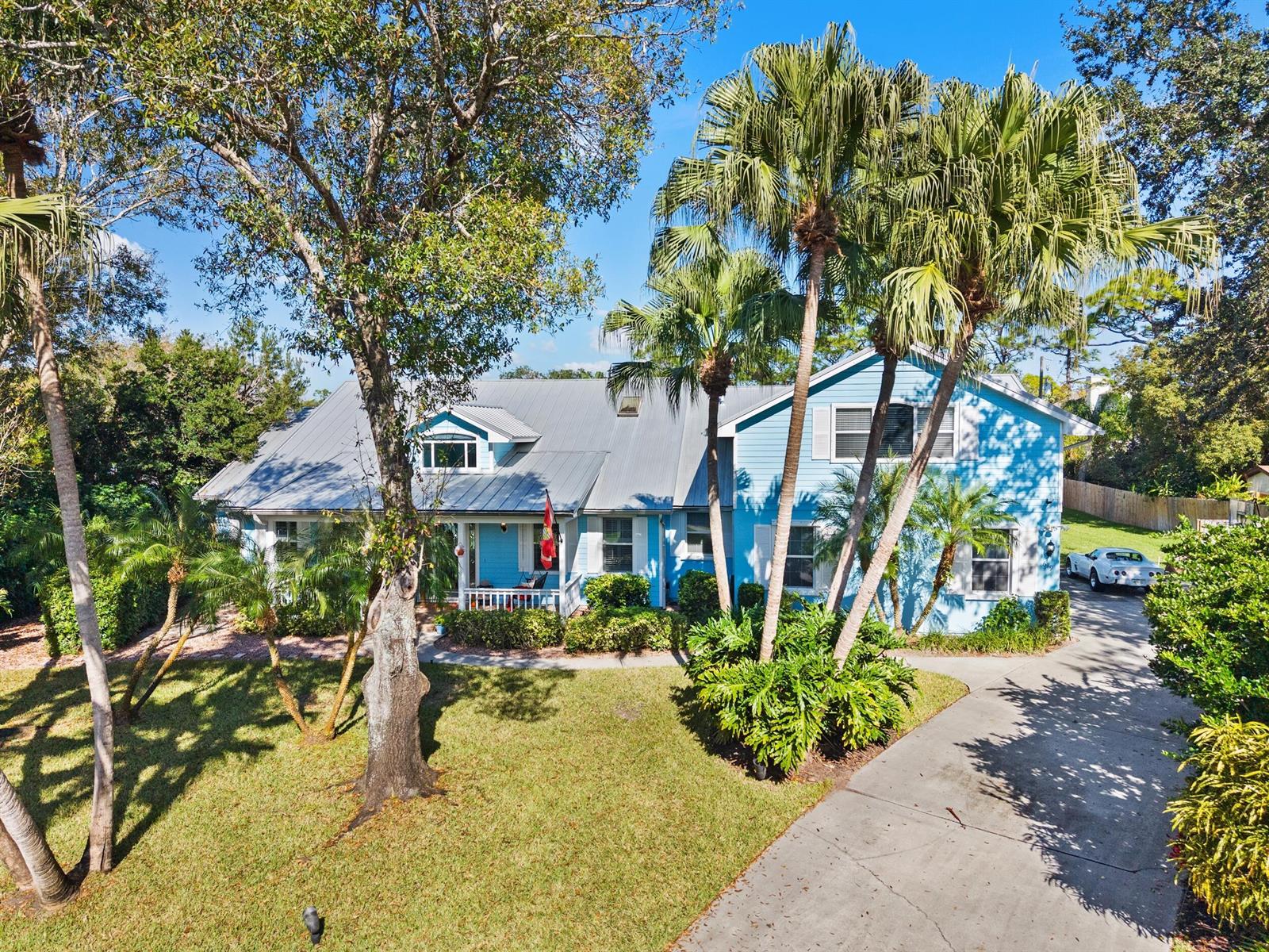 A two-story blue house with a metal roof, front porch, and palm trees in the yard — 619 Fischer Hammock Road, Sebastian FL 32958, SEBASTIAN, FL