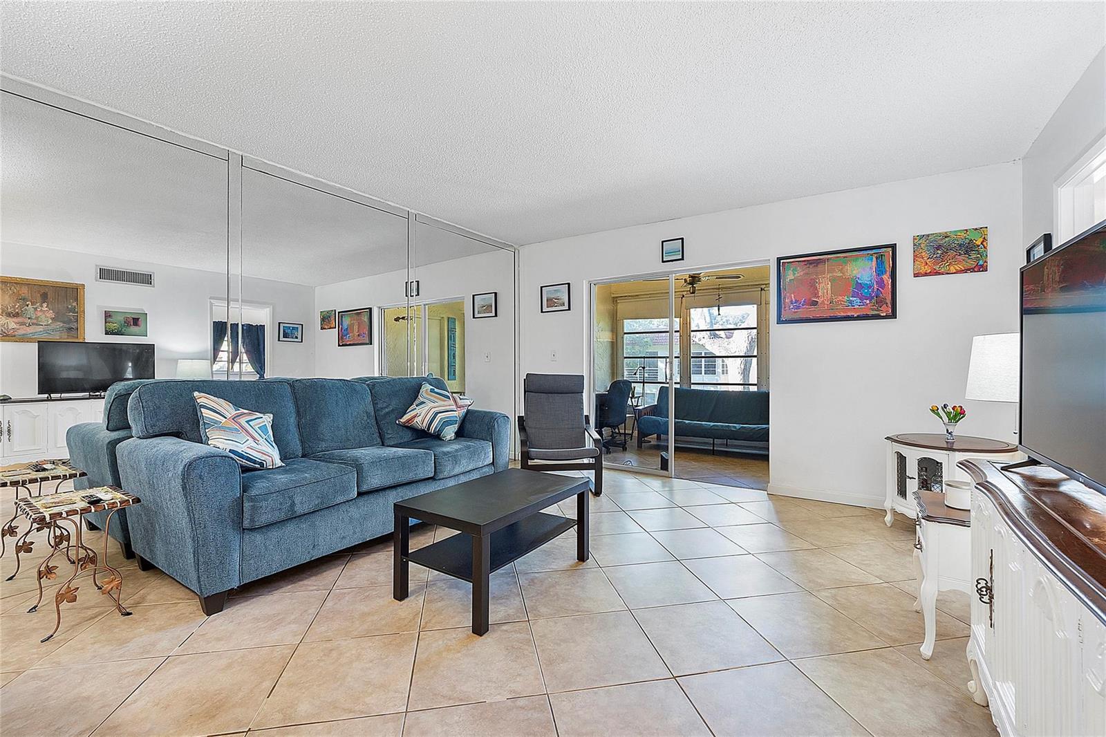 A living room features a blue sofa, tiled floors, mirrored walls, and a sliding glass door — 5621 SW 2nd Court # 201, Margate FL 33068, MARGATE, FL