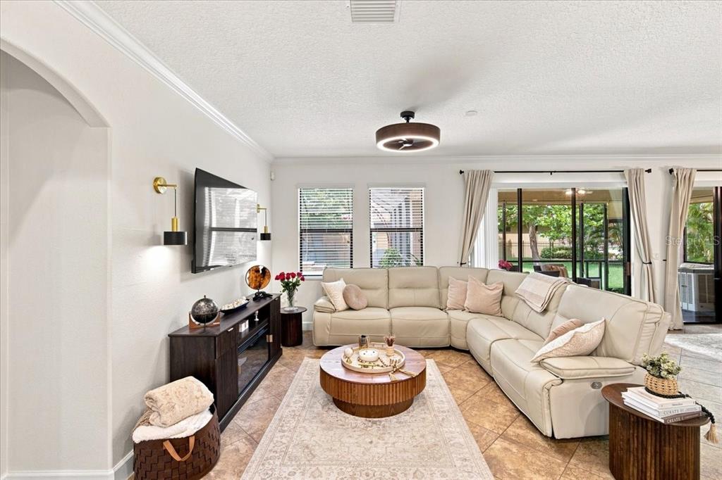 A living room features a light-colored sectional sofa, a round wooden coffee table, and tile flooring — 4508 GRAND LAKESIDE DRIVE E, PALM HARBOR, FL