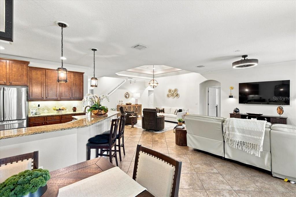 An open-concept kitchen and living area features wood cabinetry, granite countertops, and tile flooring — 4508 GRAND LAKESIDE DRIVE E, PALM HARBOR, FL