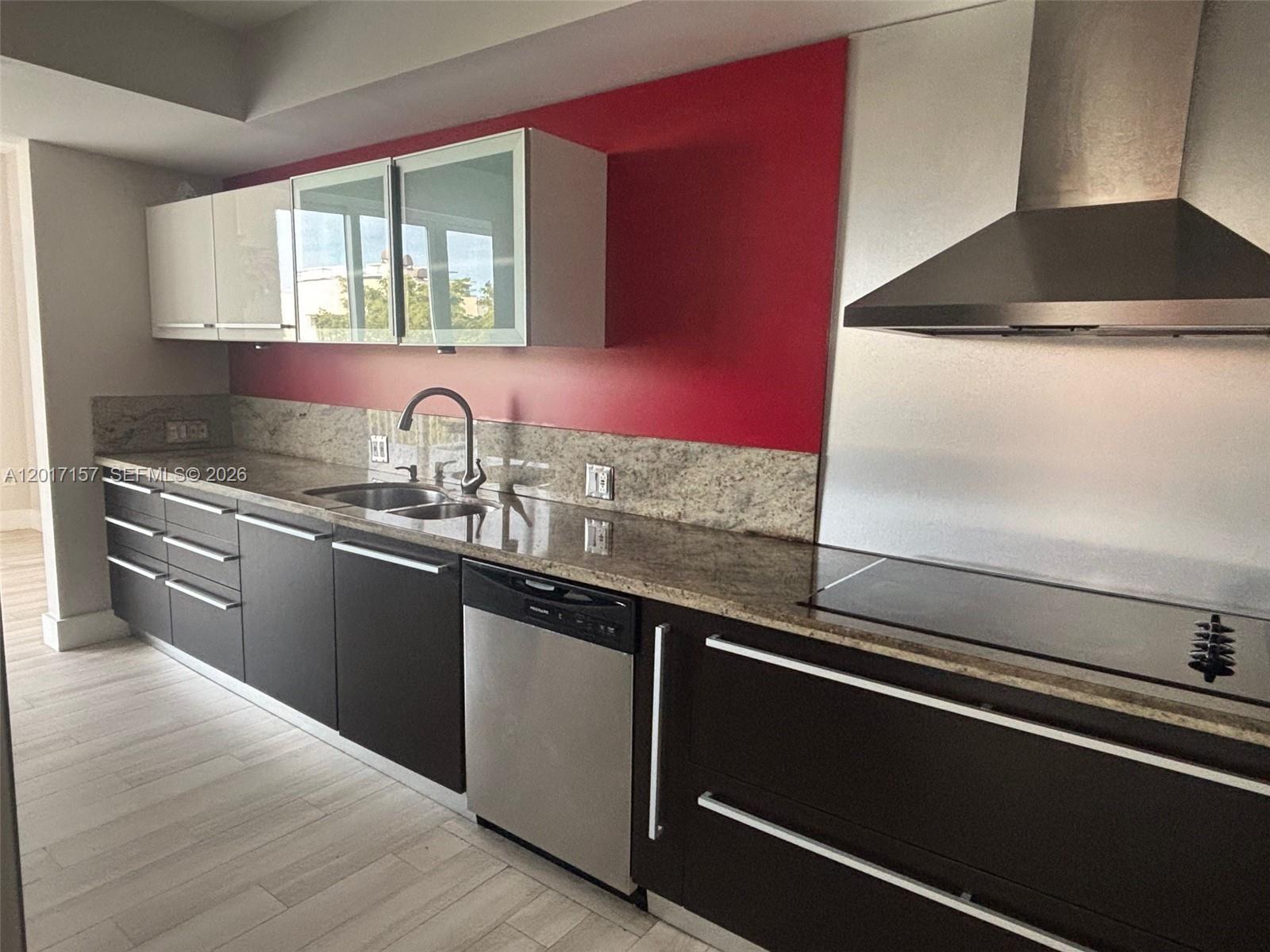 A modern kitchen features dark cabinets, a granite countertop, and a bold red accent wall — 50 Ocean Lane Dr # 404, Key Biscayne FL 33149, KEY BISCAYNE, FL