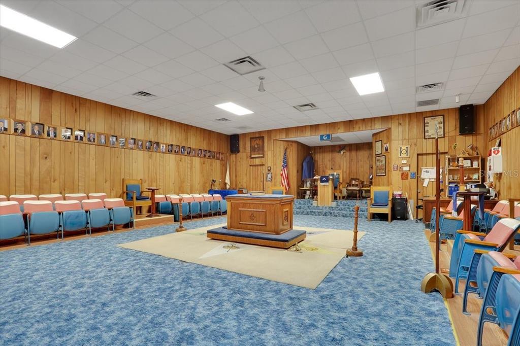 A Masonic lodge room features wood-paneled walls, blue carpeting, and rows of chairs — 18616 NW 241ST STREET, HIGH SPRINGS, FL