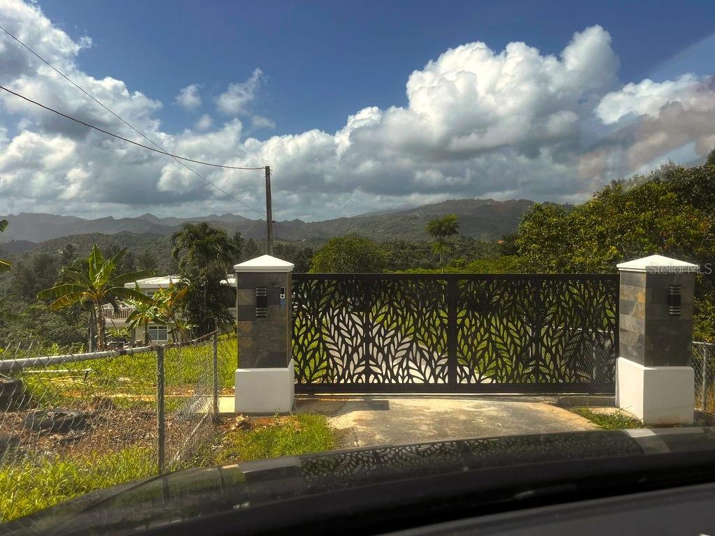 A decorative metal gate stands between two stone pillars overlooking a mountainous landscape — Solar 19 BARRIO CORDILLERA, CIALES, PR