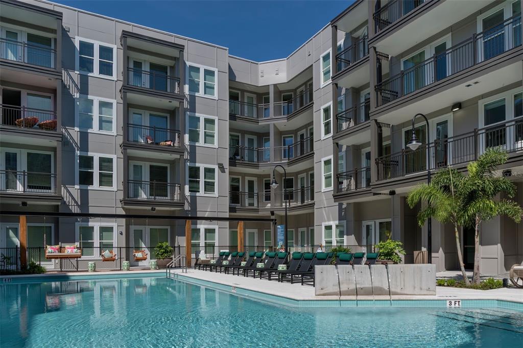 A multi-story apartment building exterior with a swimming pool and lounge chairs in the foreground — 733 MAIN LN LANE, ORLANDO, FL