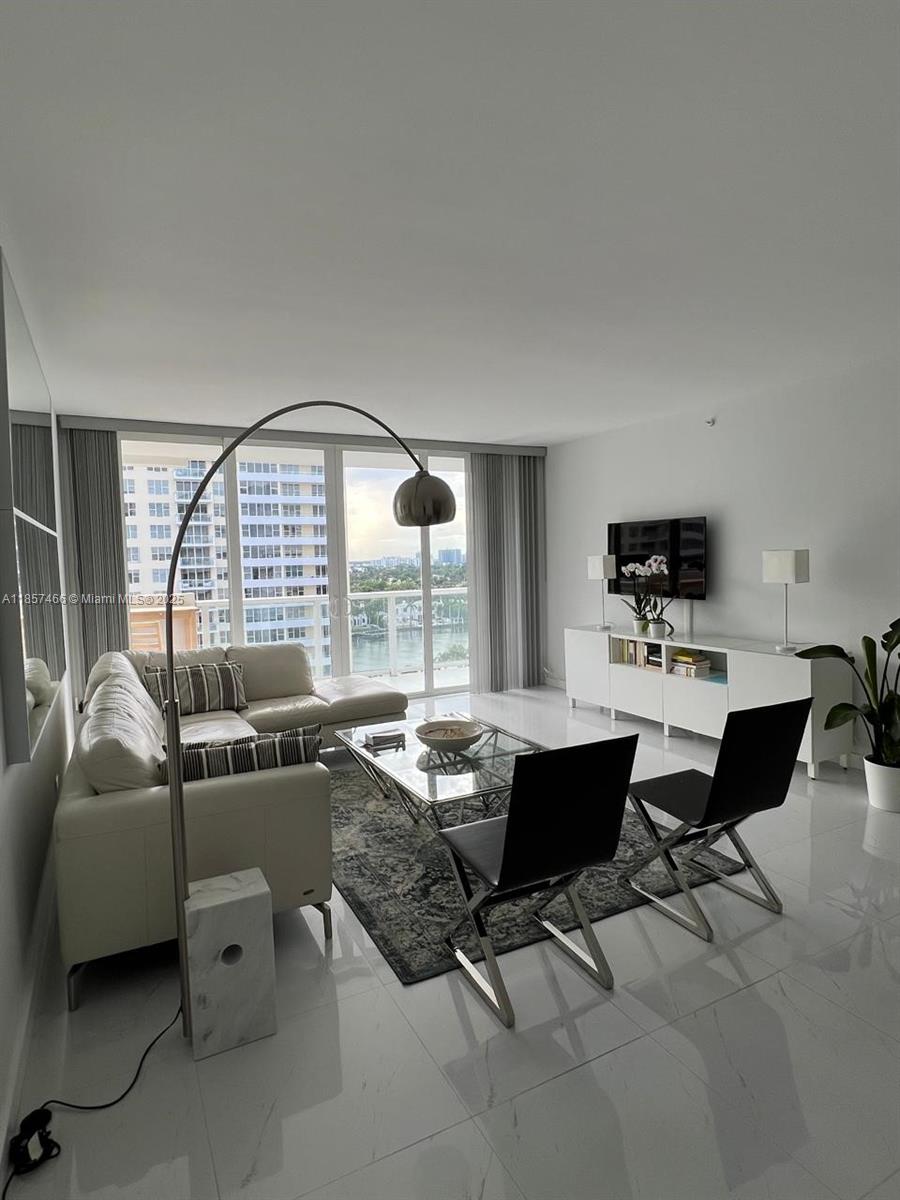 A modern living room features a white sectional sofa, glass coffee table, and floor-to-ceiling windows — 5601 Collins Ave # 1115, Miami Beach FL 33140, MIAMI BEACH, FL