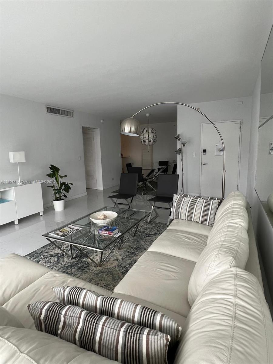 A living room features a white leather sofa, glass coffee table, and a floor lamp — 5601 Collins Ave # 1115, Miami Beach FL 33140, MIAMI BEACH, FL