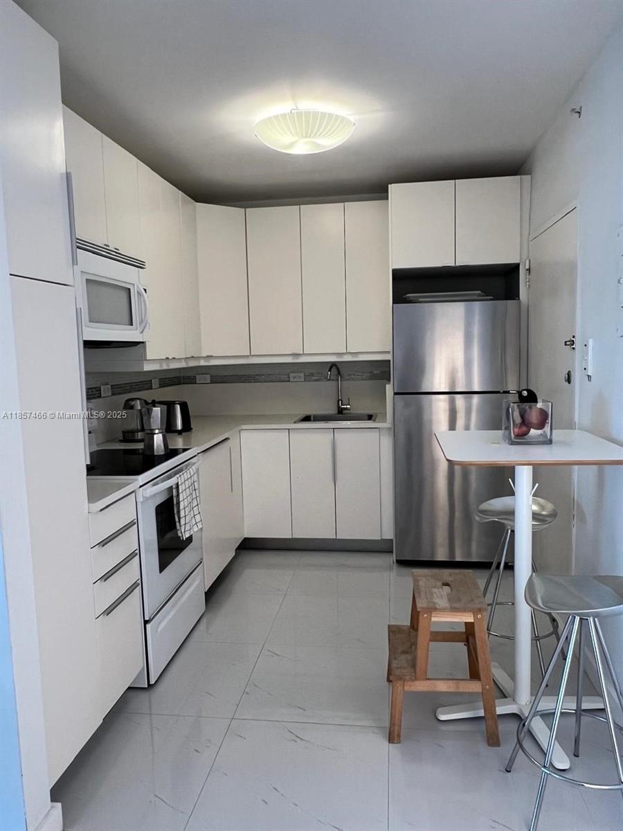 A white kitchen features stainless steel appliances, white cabinetry, and a small dining table — 5601 Collins Ave # 1115, Miami Beach FL 33140, MIAMI BEACH, FL