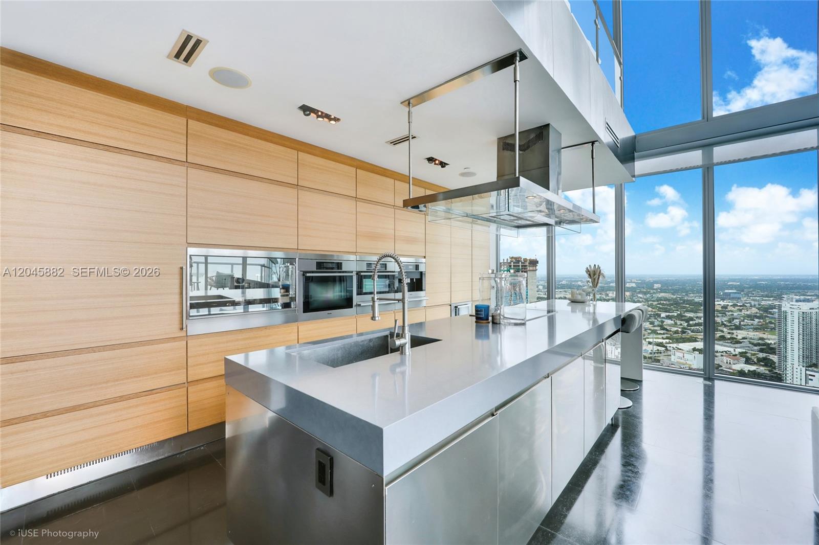 A modern kitchen features light wood cabinetry, a stainless steel island, and floor-to-ceiling windows — 888 Biscayne Blvd # 5112, Miami FL 33132, MIAMI, FL
