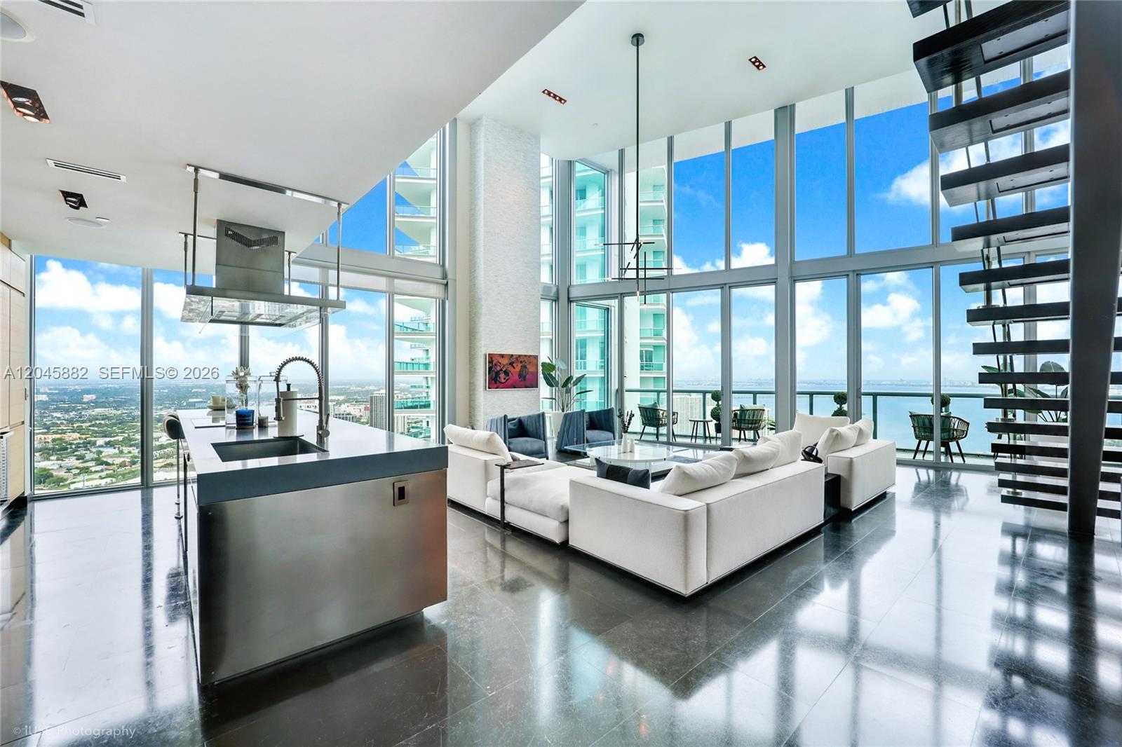 A modern, high-ceilinged living room and kitchen area with floor-to-ceiling windows overlooking the ocean — 888 Biscayne Blvd # 5112, Miami FL 33132, MIAMI, FL