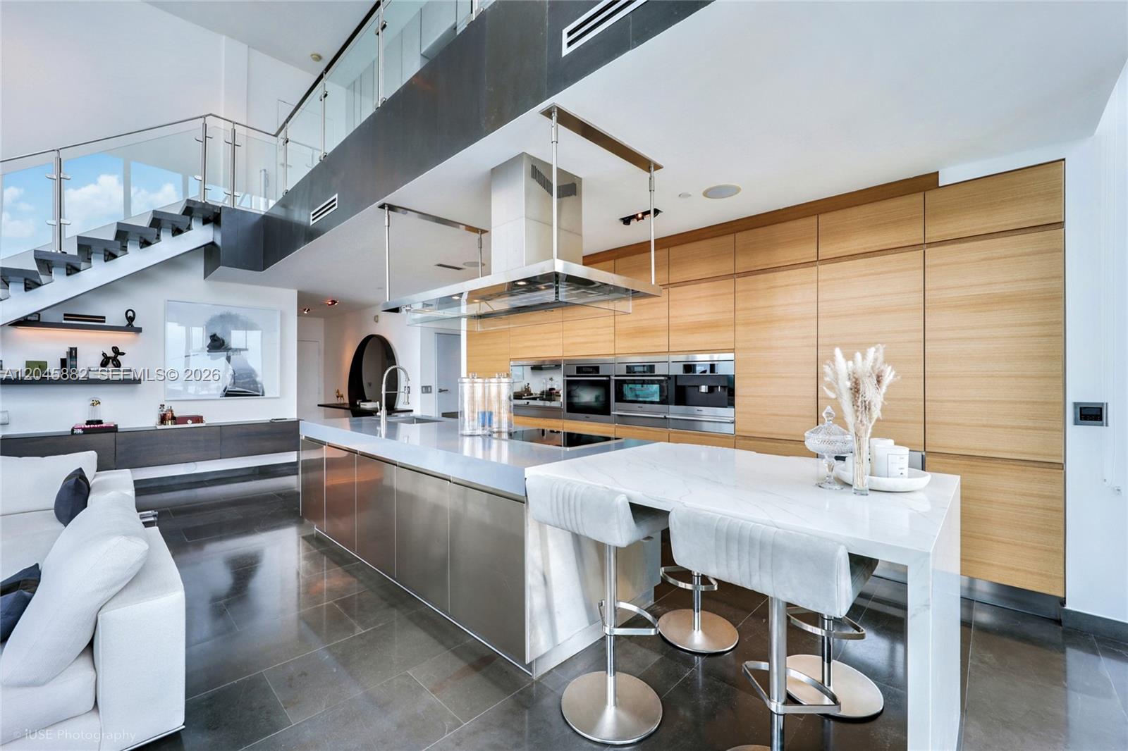 A modern kitchen features a stainless steel island, light wood cabinetry, and a floating staircase — 888 Biscayne Blvd # 5112, Miami FL 33132, MIAMI, FL