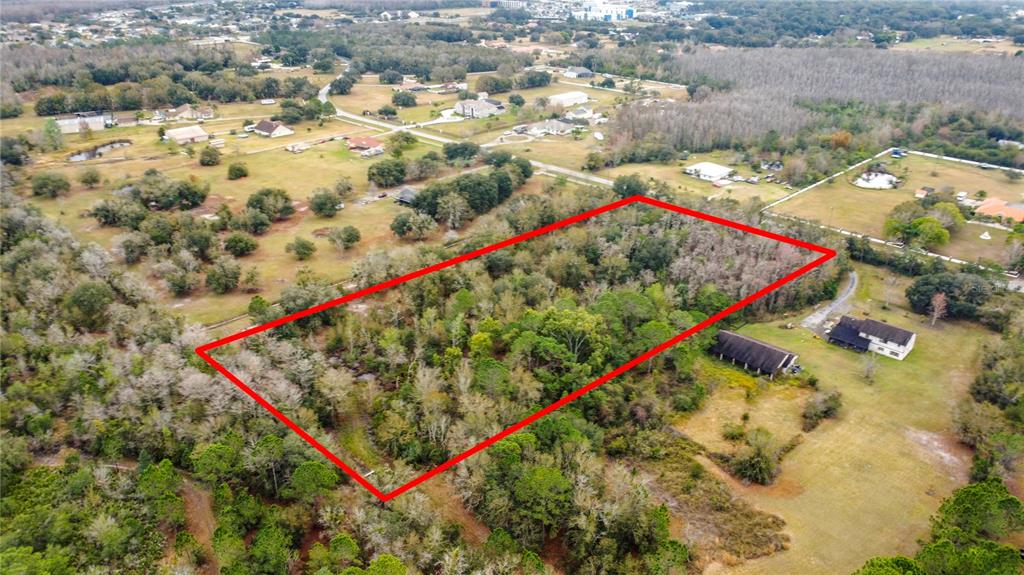 An aerial view shows a rectangular plot of land outlined in red amidst wooded terrain — TWILIGHT TRAIL, KISSIMMEE, FL