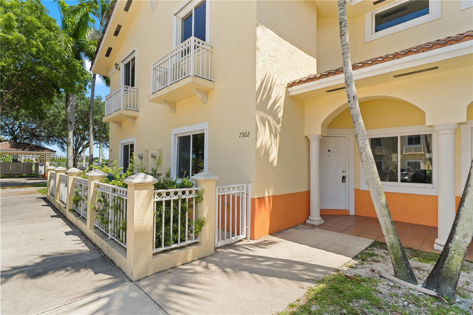 A yellow two-story townhouse features a white front door, arched entryway, and gated patio area — 7362 NW 179th Ter # 7362, Hialeah FL 33015, HIALEAH, FL