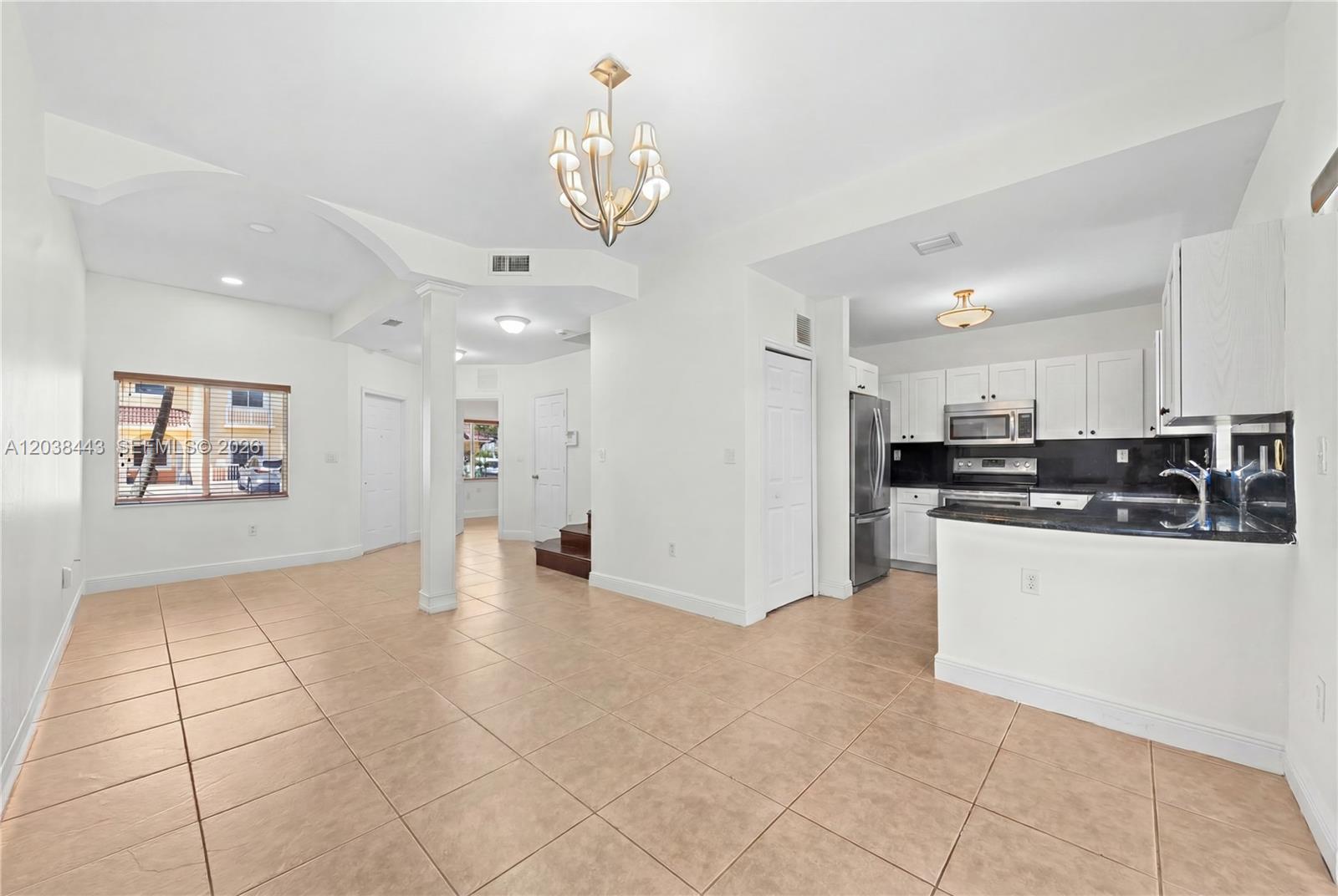 A bright, open-concept kitchen and living area features white cabinetry, tile flooring, and a chandelier — 7362 NW 179th Ter # 7362, Hialeah FL 33015, HIALEAH, FL
