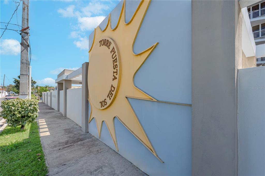 A large yellow sun-shaped sign for Torre Puesta del Sol is mounted on a wall — SR 102 km 14.6 BARRIO JOYUDA COND TORRE PUESTA DEL SOL UNIT 406, CABO ROJO, PR