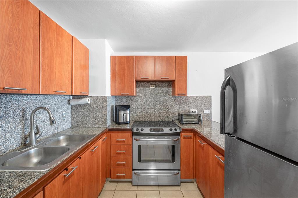 A kitchen features wood cabinets, granite countertops, stainless steel appliances, and a double sink — SR 102 km 14.6 BARRIO JOYUDA COND TORRE PUESTA DEL SOL UNIT 406, CABO ROJO, PR