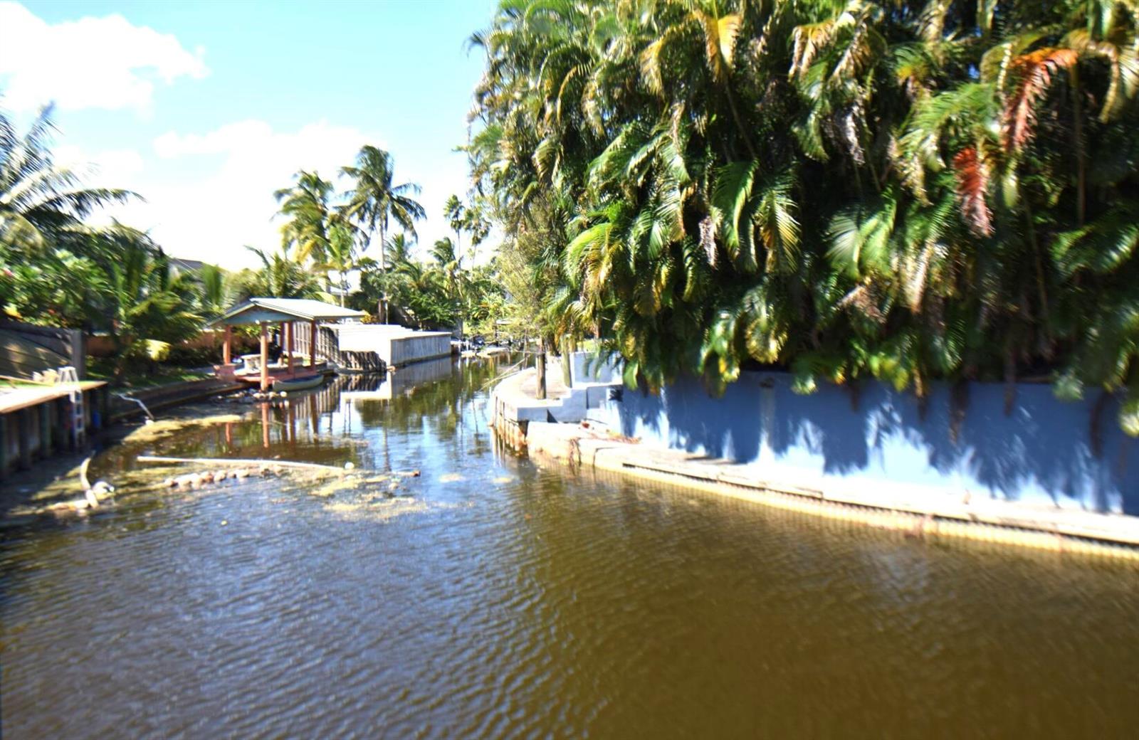 A canal view showing a wooden boat dock, palm trees, and a blue retaining wall — 2215 Hypoluxo Rd Road, Lantana FL 33462, LANTANA, FL