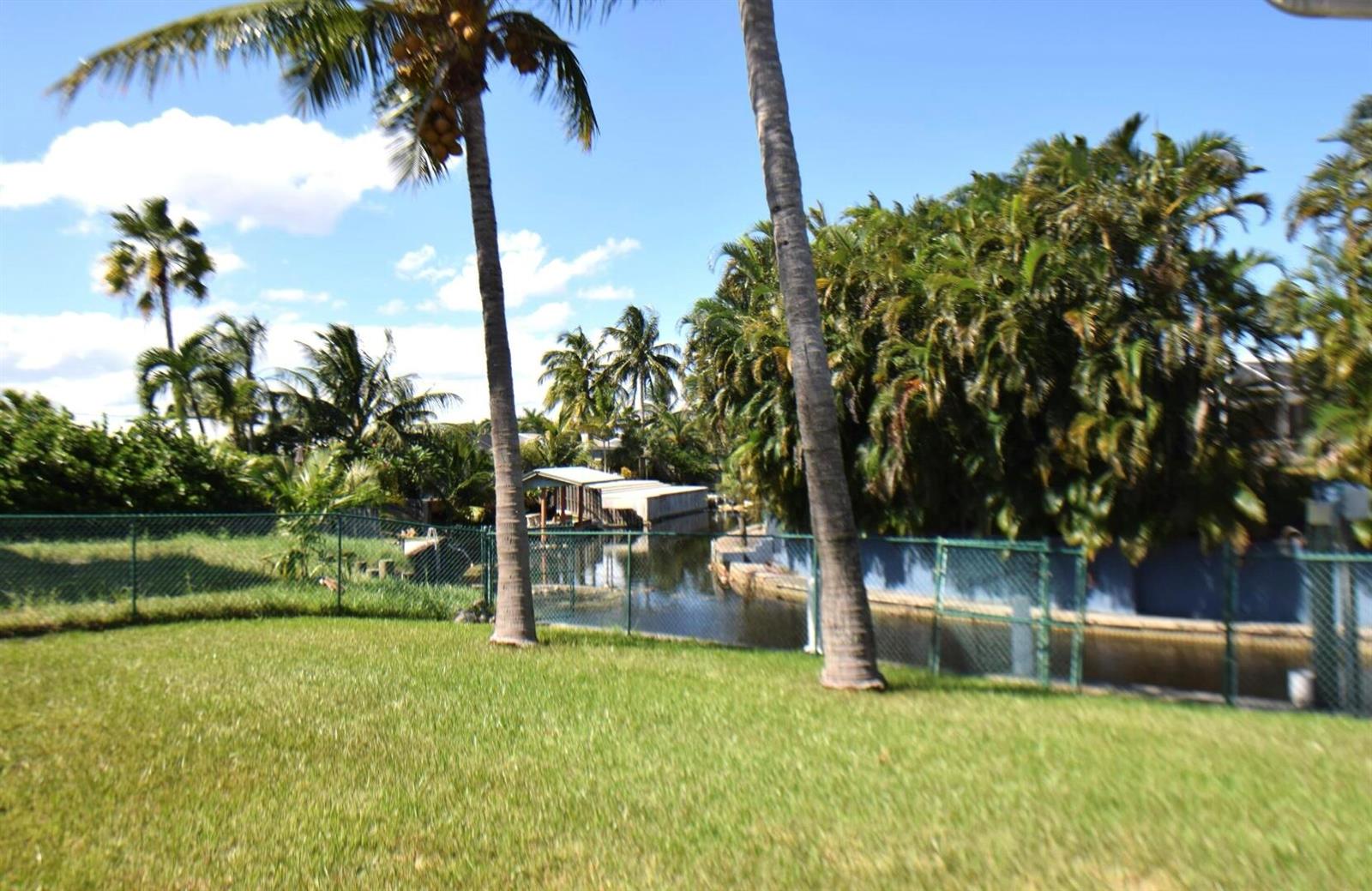 A grassy backyard features two tall palm trees and a chain-link fence bordering a canal — 2215 Hypoluxo Rd Road, Lantana FL 33462, LANTANA, FL