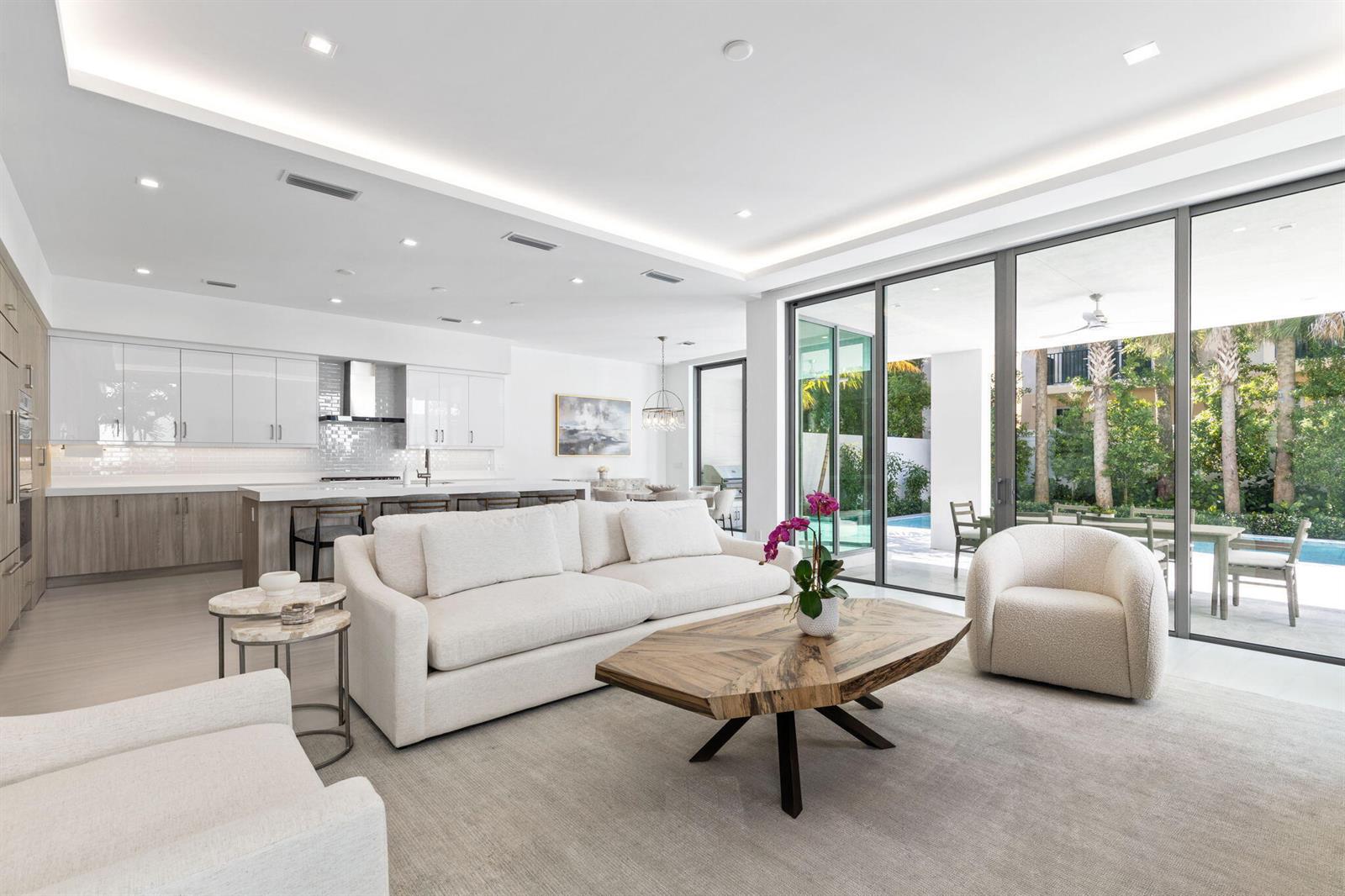 A modern open-concept living room features a white sofa, wood coffee table, and sliding glass doors — 406 Ocean One Lane, Juno Beach FL 33408, JUNO BEACH, FL