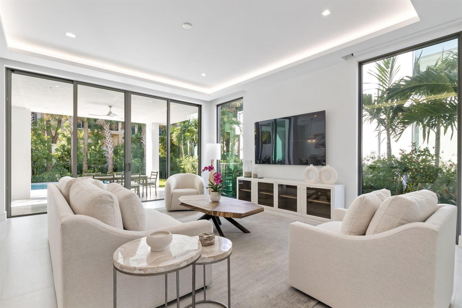 A bright living room features white furniture, a wood coffee table, and large glass sliding doors — 406 Ocean One Lane, Juno Beach FL 33408, JUNO BEACH, FL