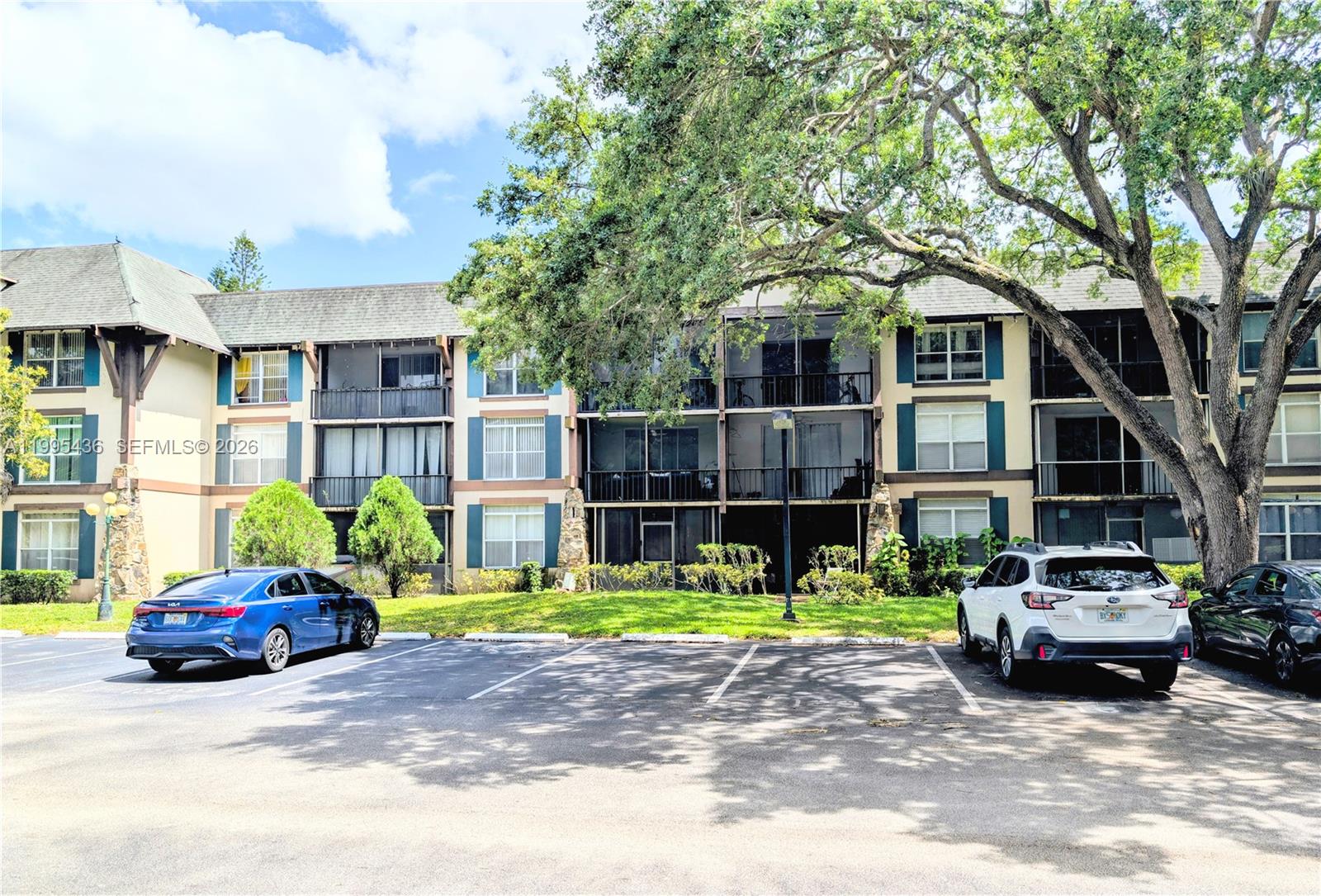 A three-story apartment building with screened balconies sits behind a parking lot with cars — 3720 Inverrary Dr # 1J, Lauderhill FL 33319, LAUDERHILL, FL