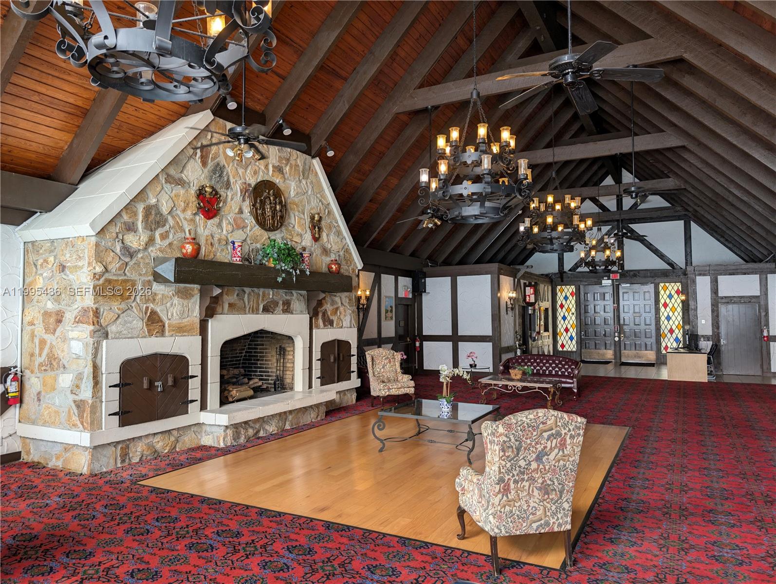 A large room features a stone fireplace, vaulted wood-beamed ceilings, and patterned red carpeting — 3720 Inverrary Dr # 1J, Lauderhill FL 33319, LAUDERHILL, FL