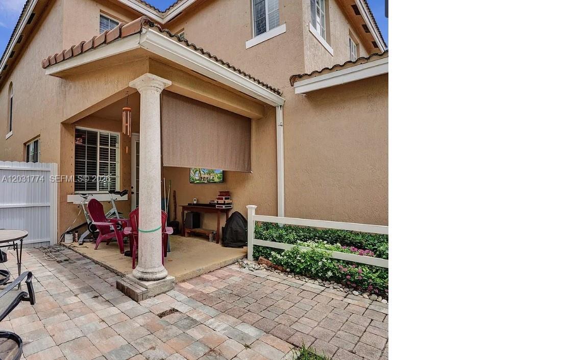A covered patio with a stone pillar, brick pavers, and a white vinyl fence — HOMESTEAD, FL